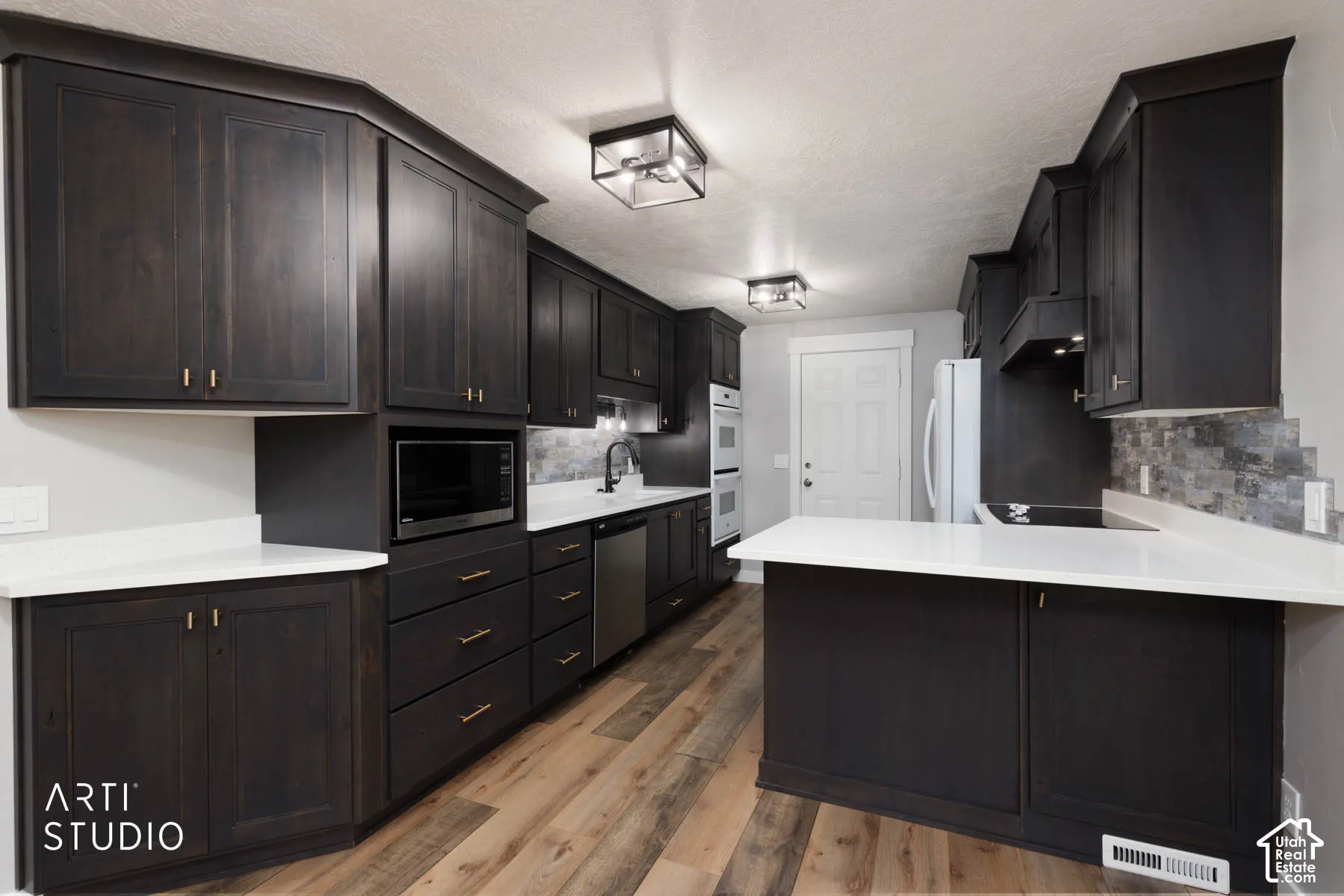 Dark wood-finish cabinetry, light countertops, wood-finish flooring, built-in double oven, and stainless steel appliances
