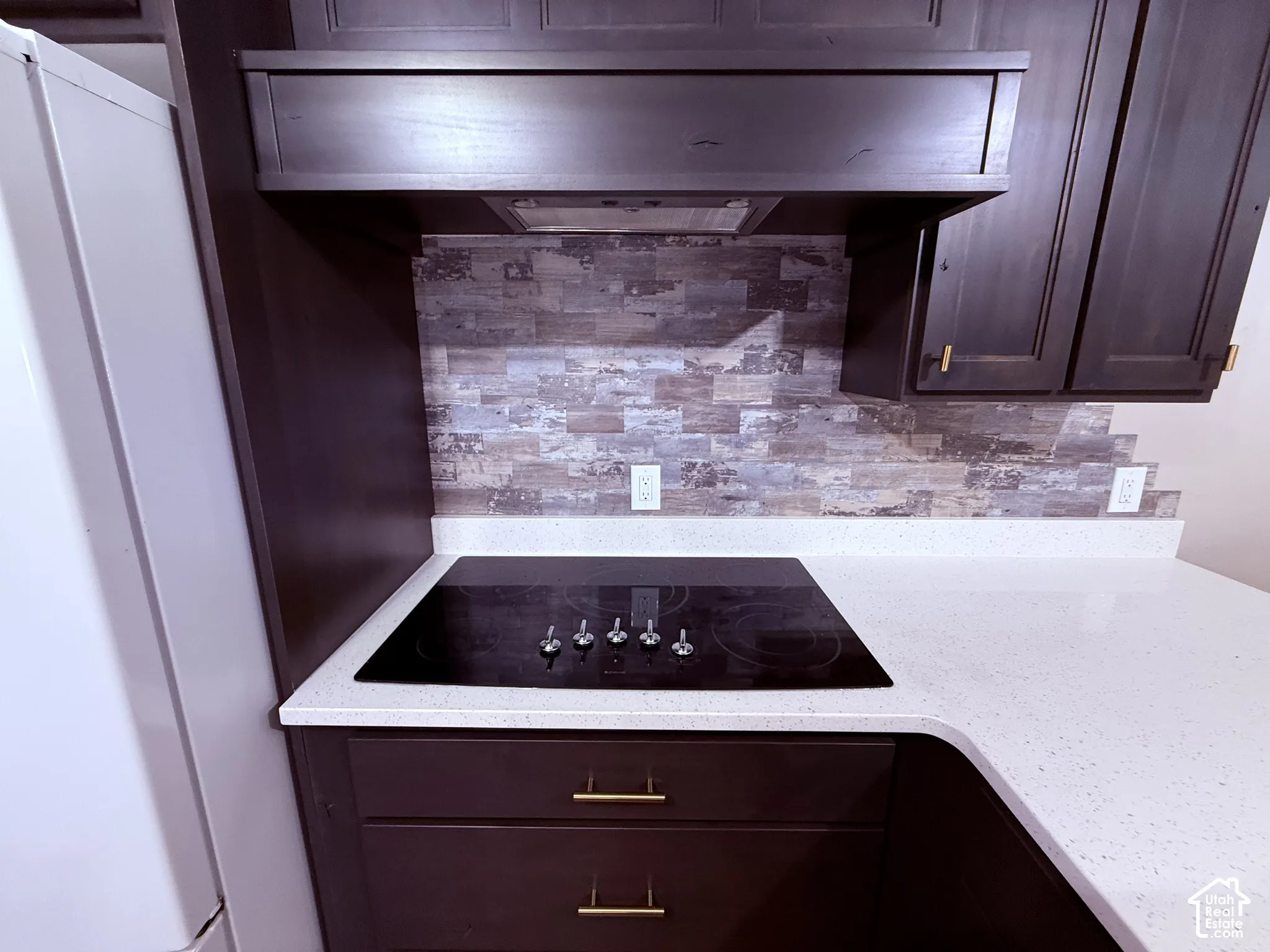 Built-in cooktop with a white solid surface countertop, dark wood-finish cabinetry, and a textured tile backsplash