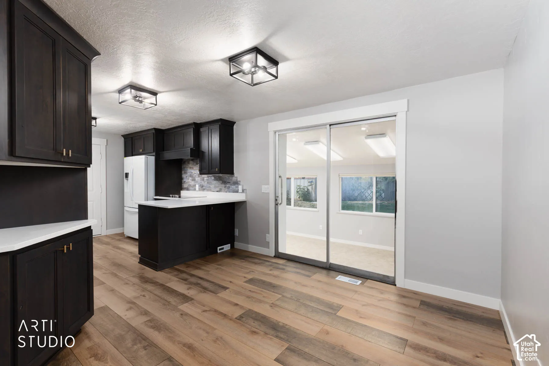 Kitchen featuring wood-finish flooring, dark cabinetry with gold-tone hardware, white countertops, and a tiled backsplash