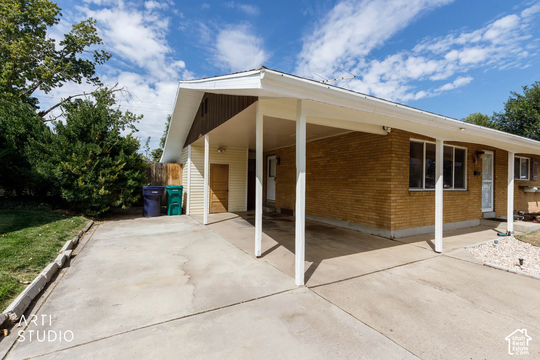 Attached carport with concrete driveway, brick exterior, and mature landscaping
