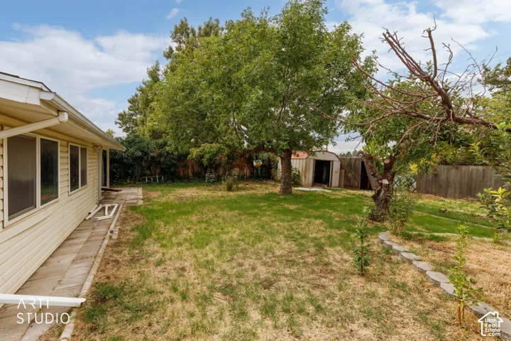 Expansive backyard featuring mature trees, a storage shed, and a privacy fence