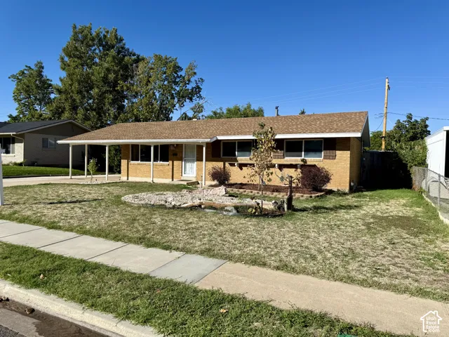 Brick exterior with a covered carport, mature landscaping, and a sidewalk
