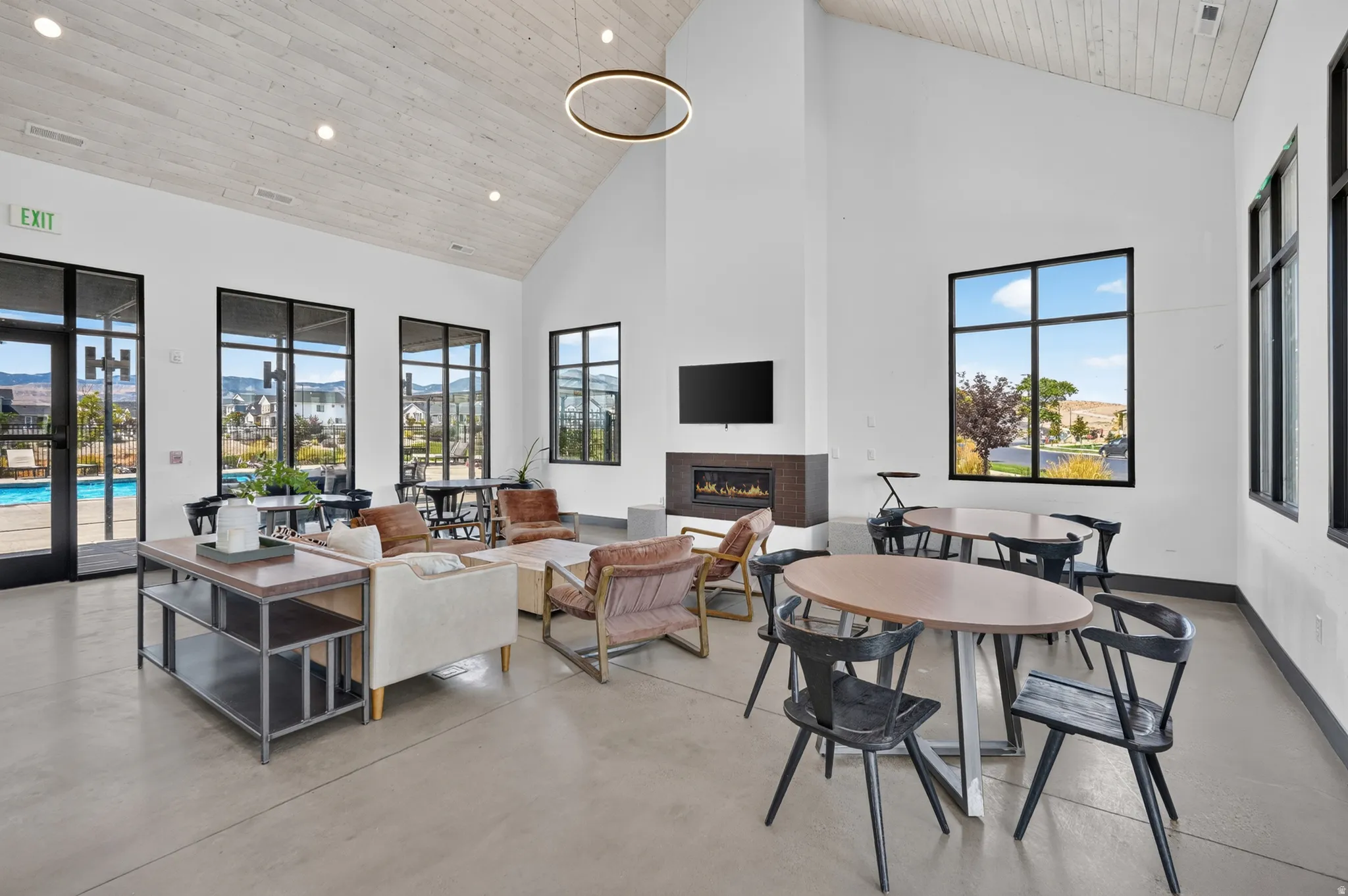 Vaulted ceiling with wood-finish paneling, contemporary chandelier, gas fireplace with stone-finish surround, large windows with black frames, and polished concrete flooring