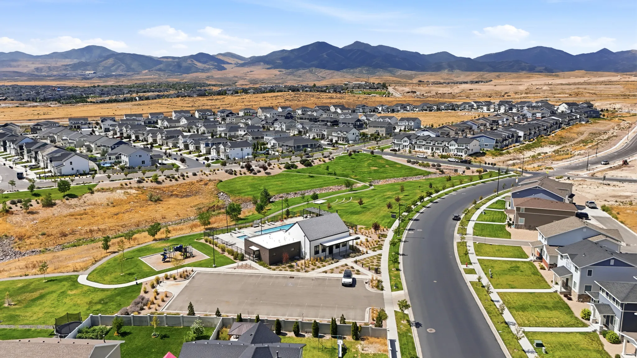 Expansive residential community with diverse home exteriors, a community pool, and a children's play area, all surrounded by natural landscaping and distant mountains