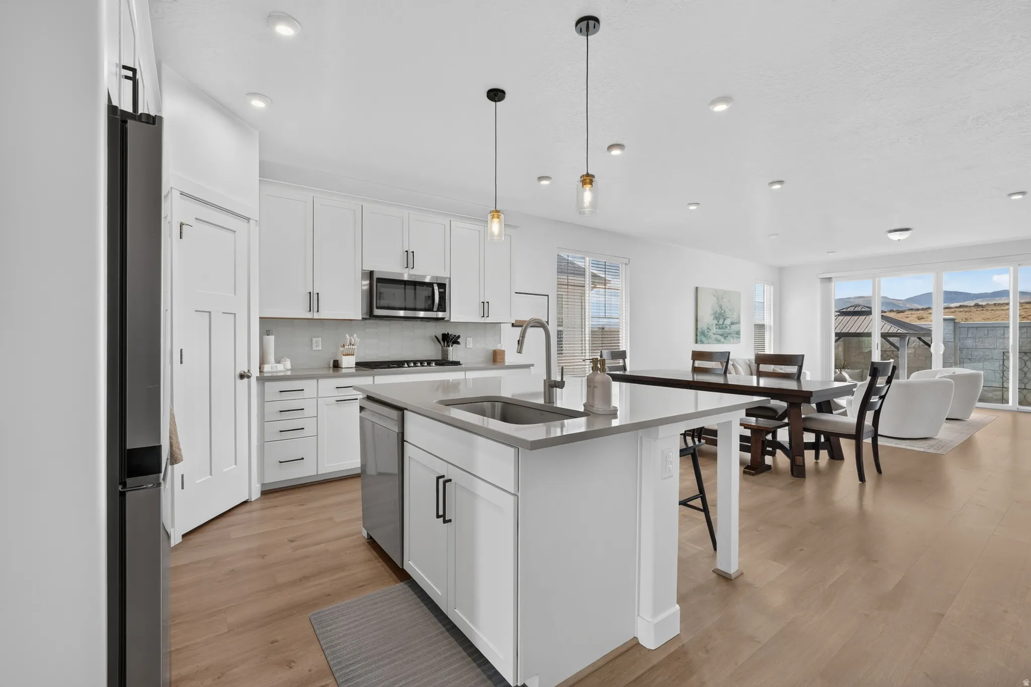 Modern kitchen featuring white cabinetry, stainless steel appliances, a center island with sink, and wood-finish flooring