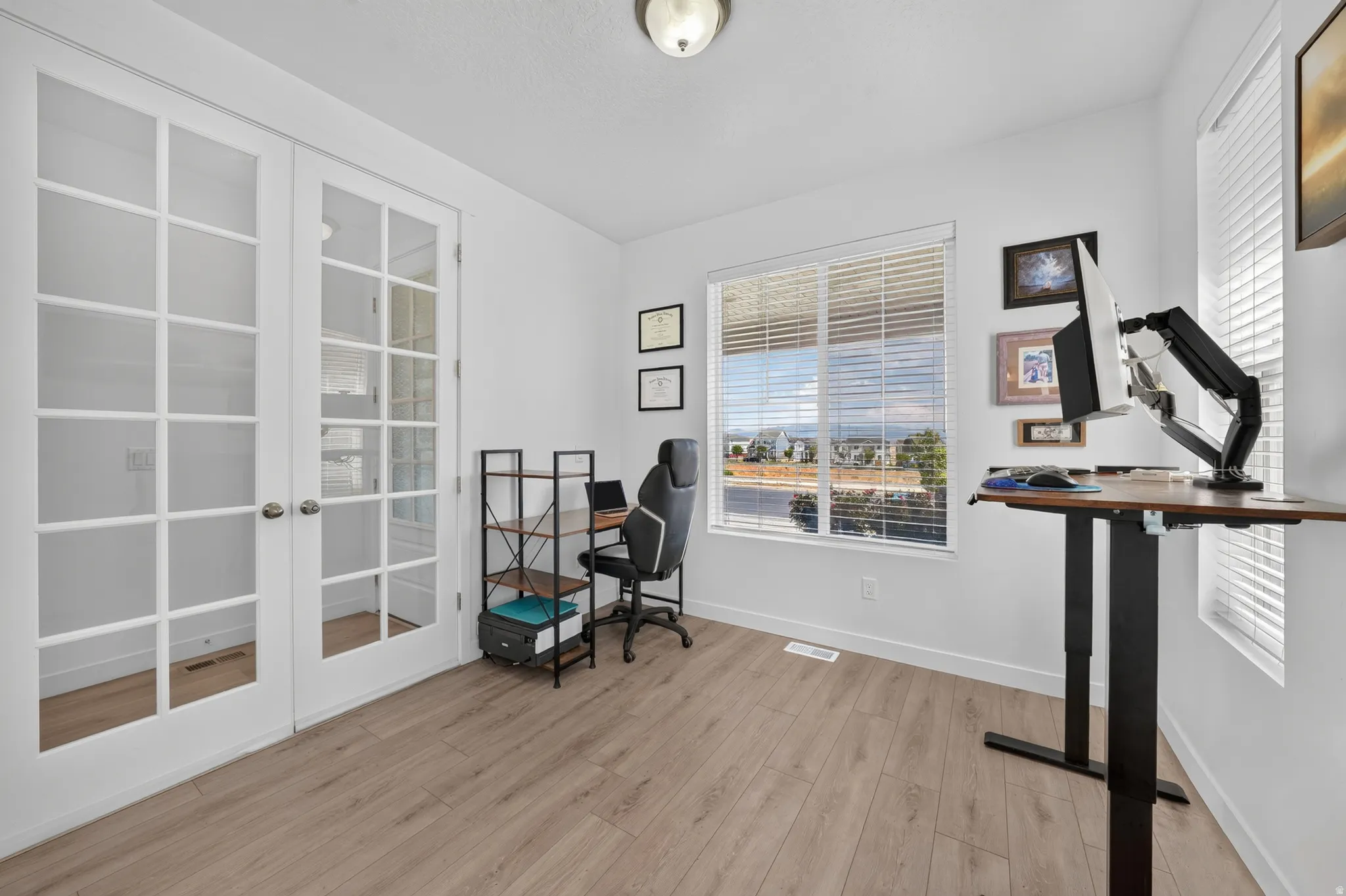White walls, wood-finish flooring, two large windows, and a ceiling-mounted light fixture