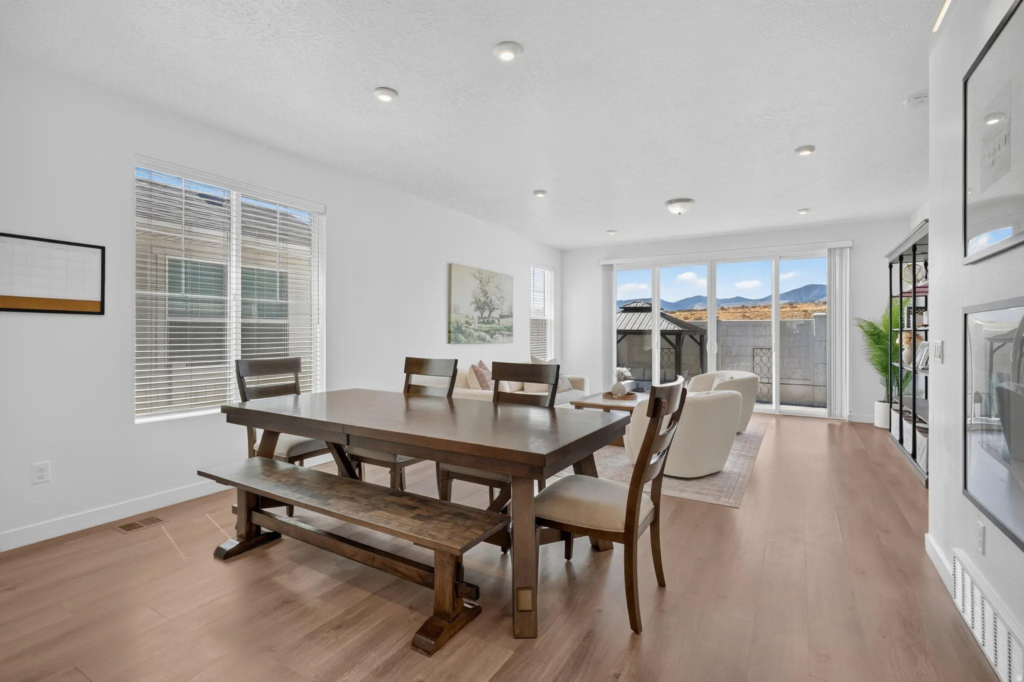 Open-concept dining and living area featuring wood-finish flooring, recessed lighting, expansive windows, and a sliding glass door