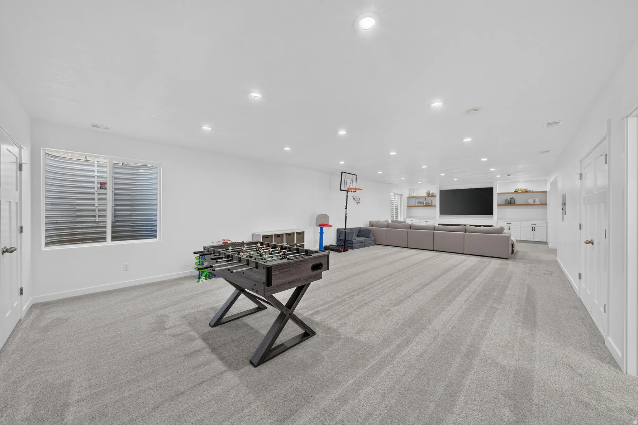 Spacious living area featuring light gray carpeting, recessed lighting, and a window with a window well