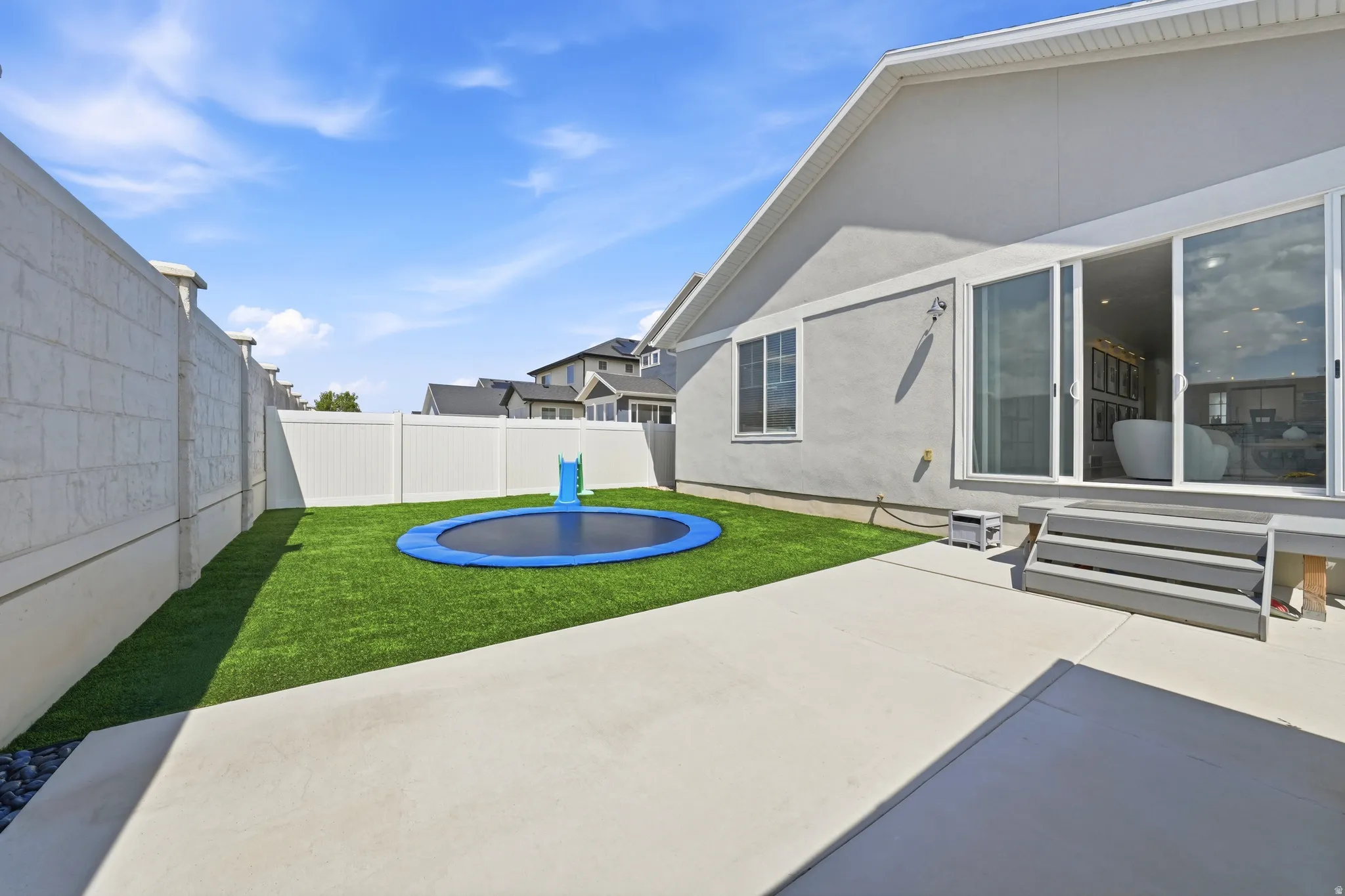 Concrete patio with steps leading to a sliding glass door, artificial turf, and privacy fencing
