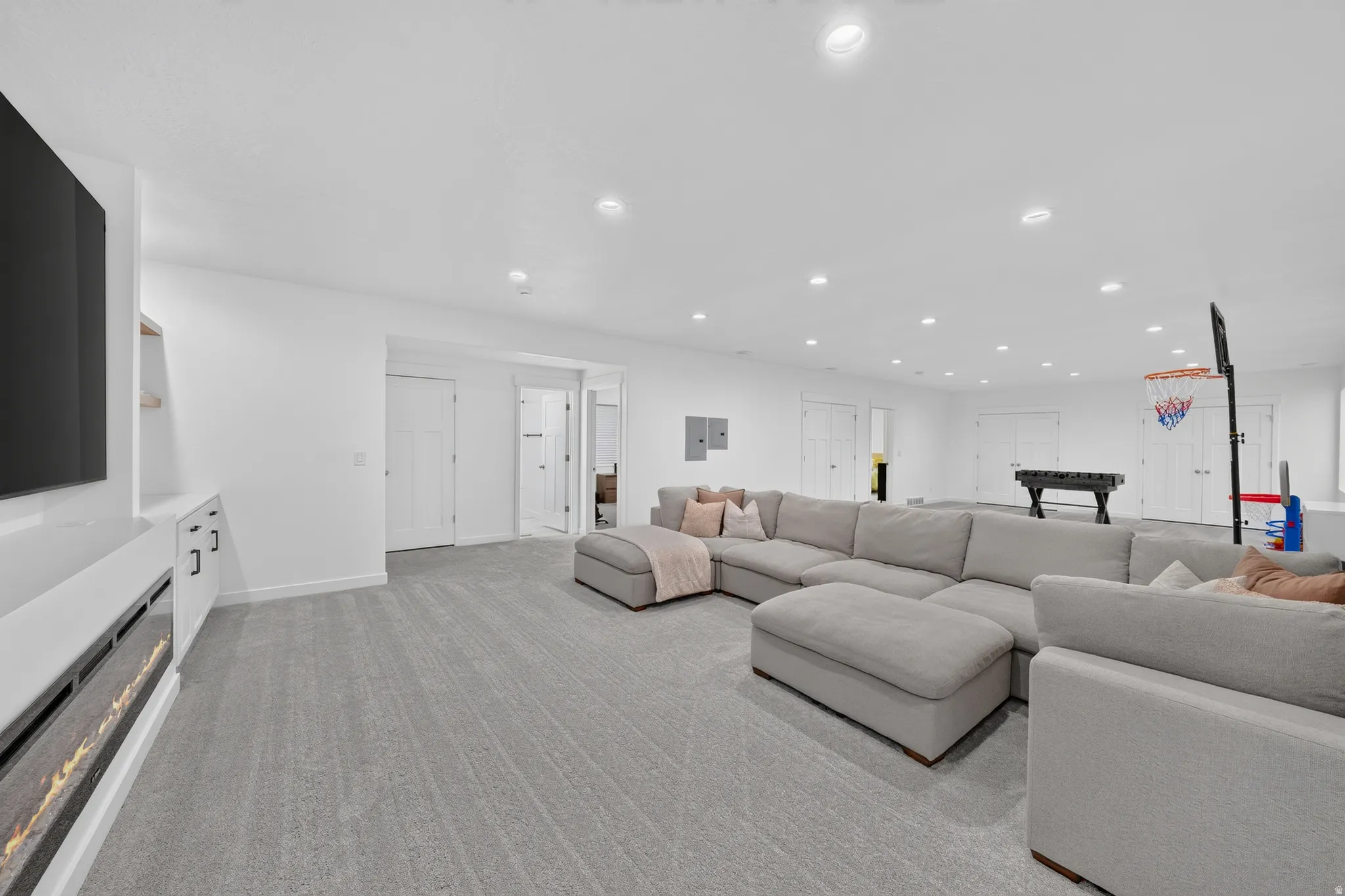 Spacious room featuring light gray carpeting, recessed lighting, white walls, and built-in media cabinetry with an integrated linear fireplace
