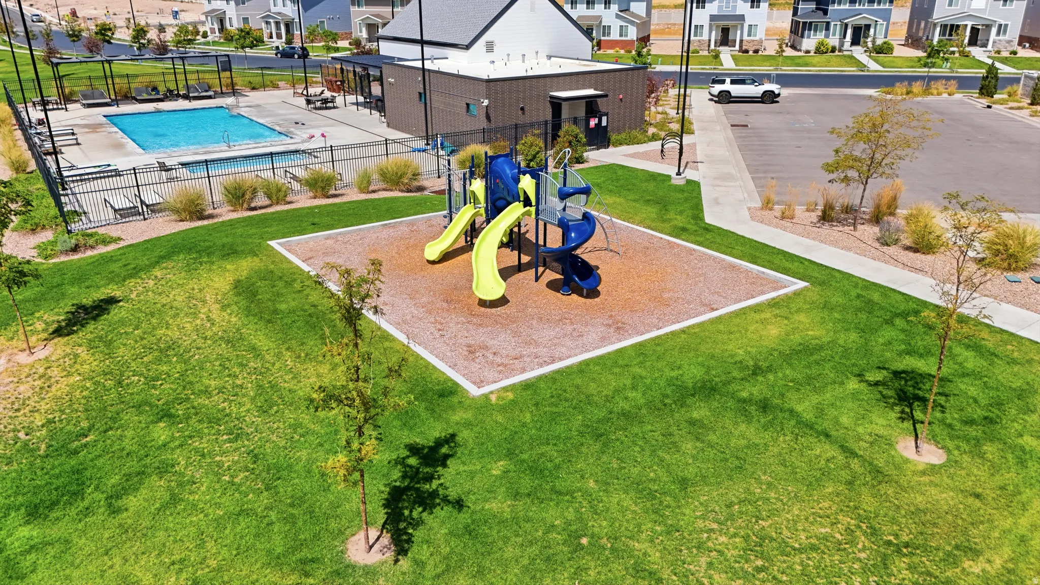 Manicured green space featuring a playground with slides, an outdoor swimming pool, and a building with a covered patio