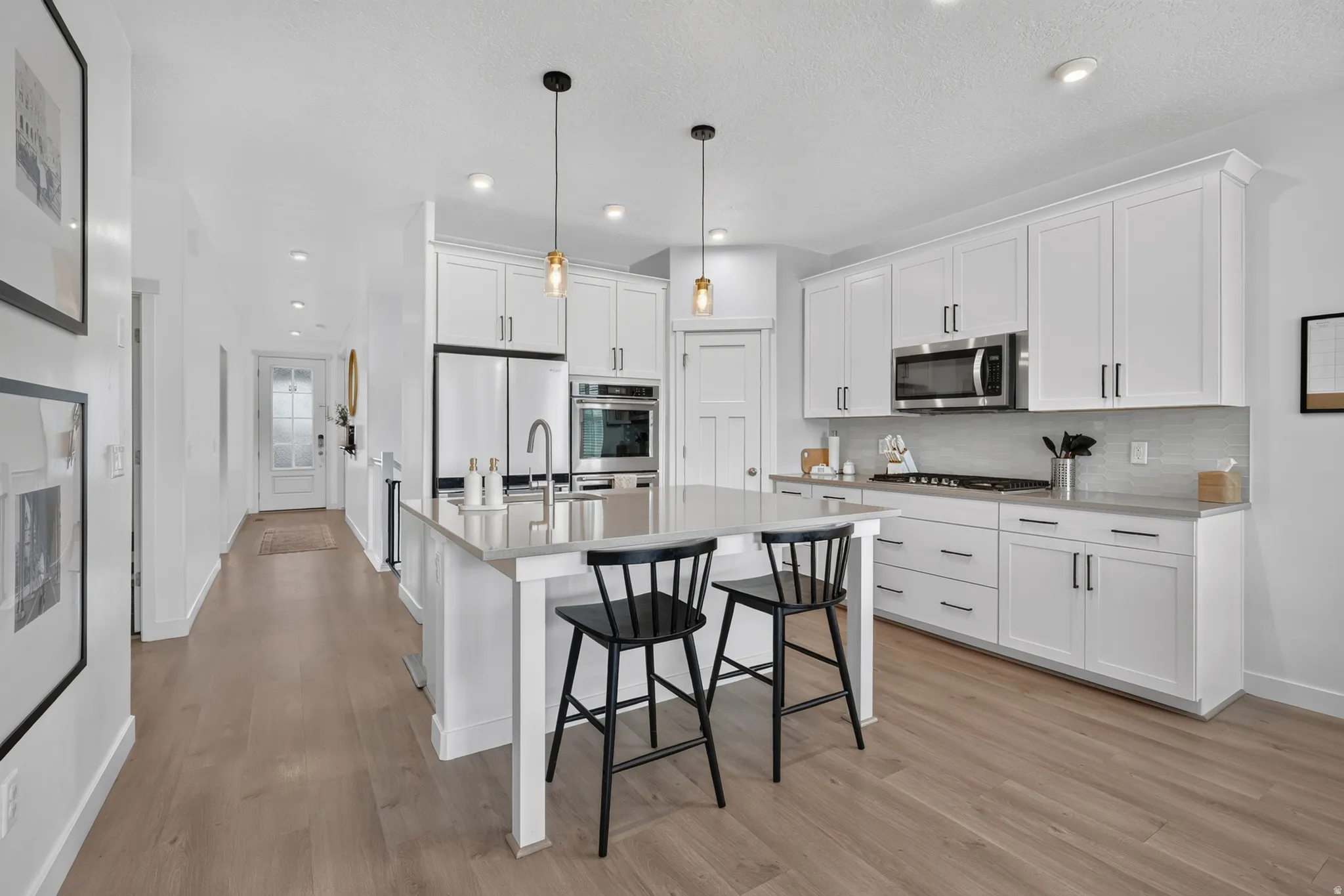Modern kitchen featuring white shaker cabinetry, stainless steel appliances, a light-toned backsplash, a central island with a sink, and wood-finish flooring