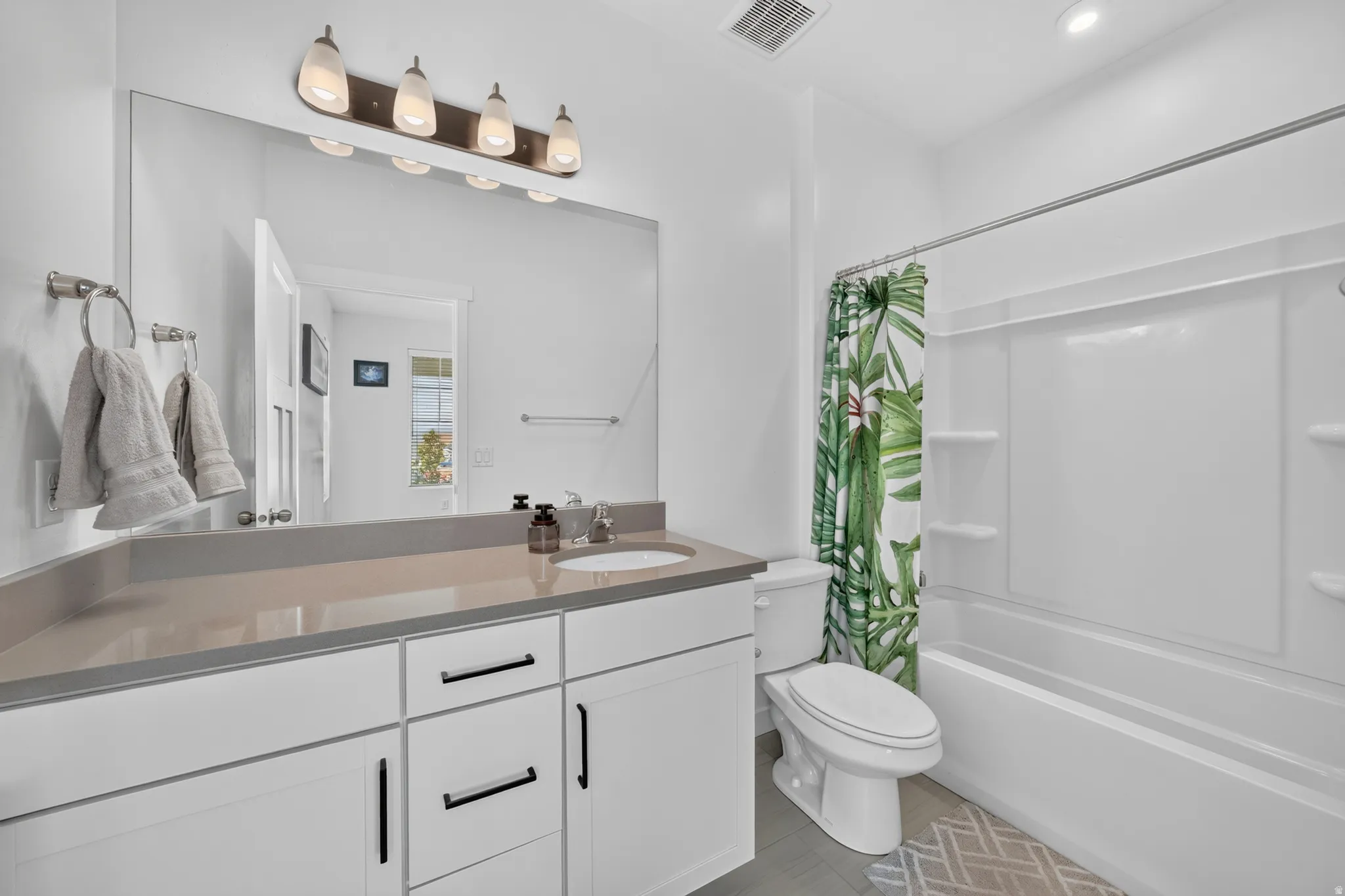 White vanity with dark hardware, a light-colored countertop, and a large mirror