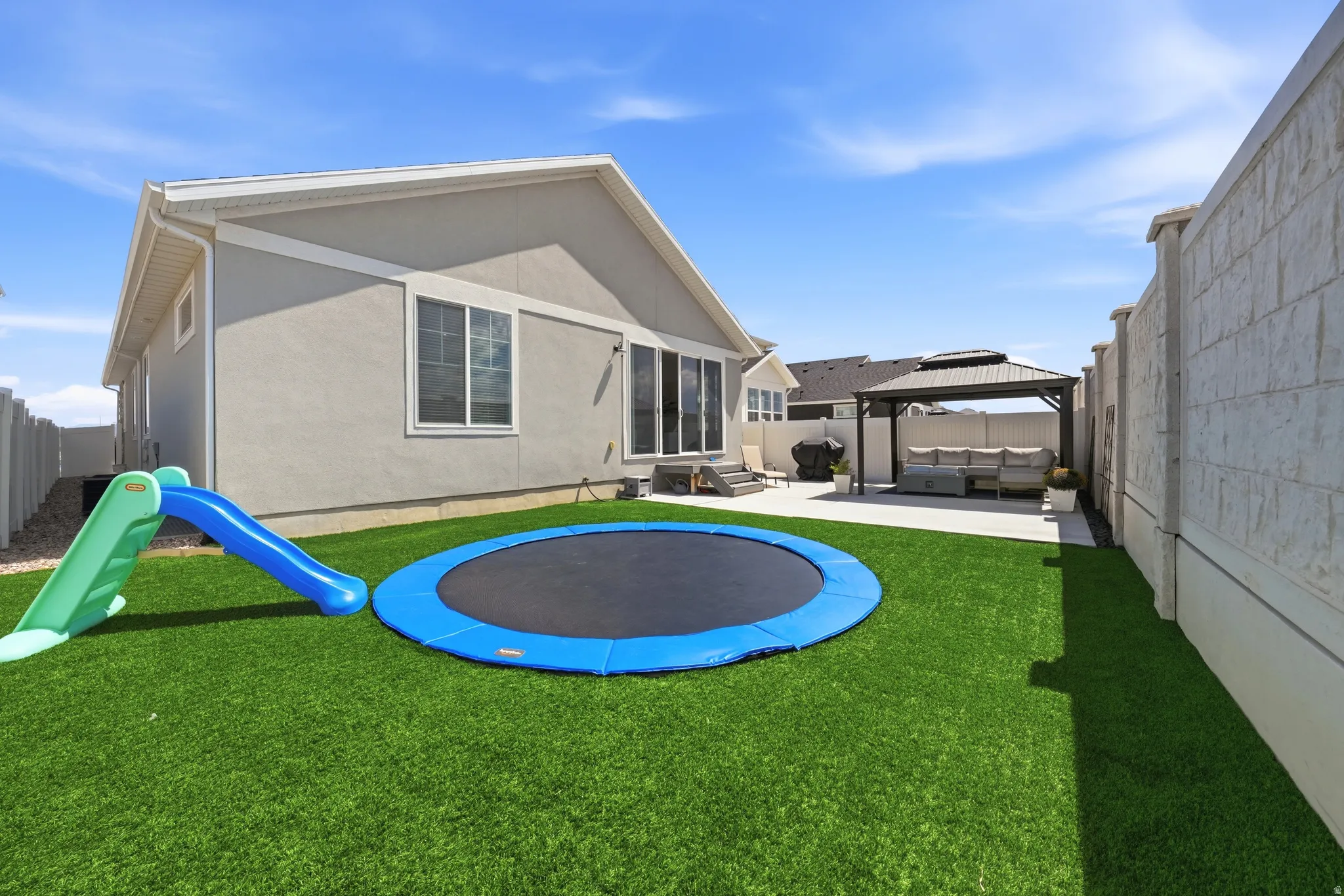 Expansive backyard featuring artificial turf, a concrete patio, a metal-framed gazebo, and a block retaining wall