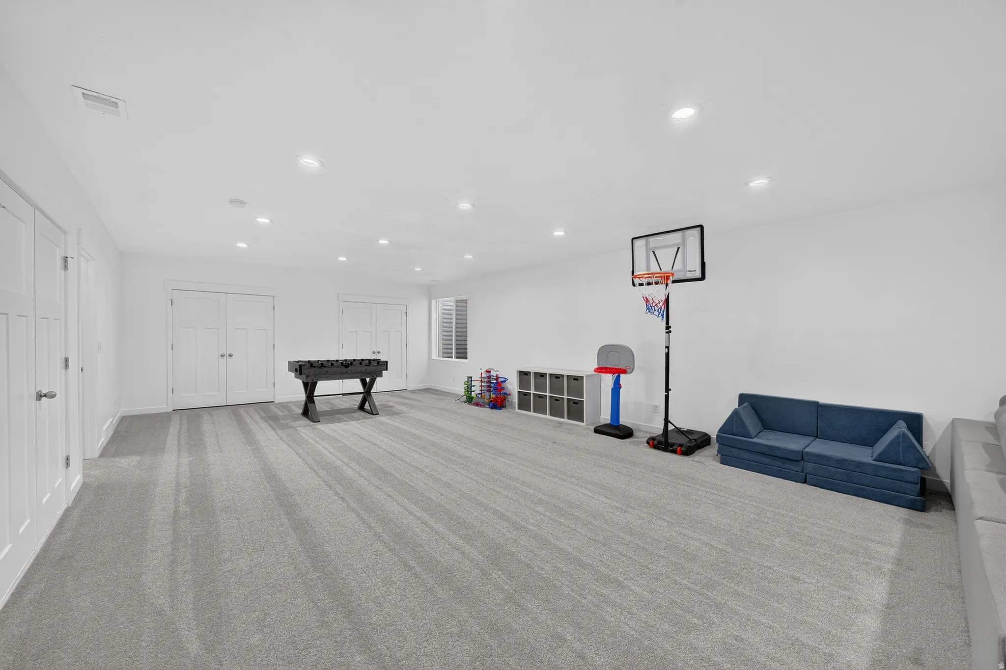 Spacious room featuring light gray carpeting, recessed ceiling lighting, and multiple white paneled doors