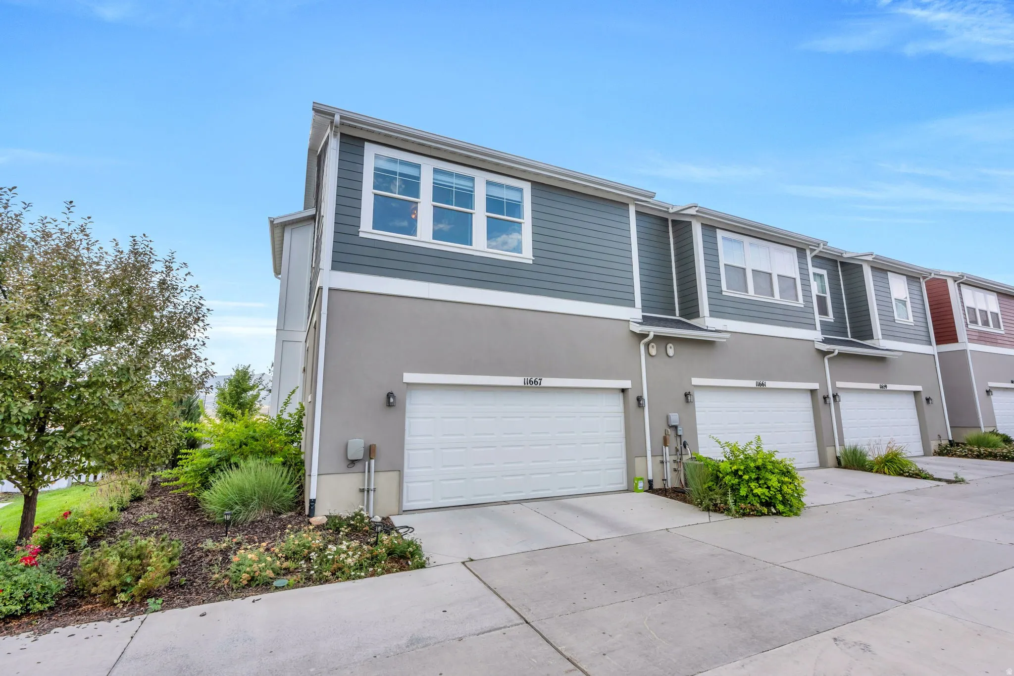 Contemporary townhome exterior with horizontal siding, stucco facade, multiple garage doors, concrete driveways, and landscaping