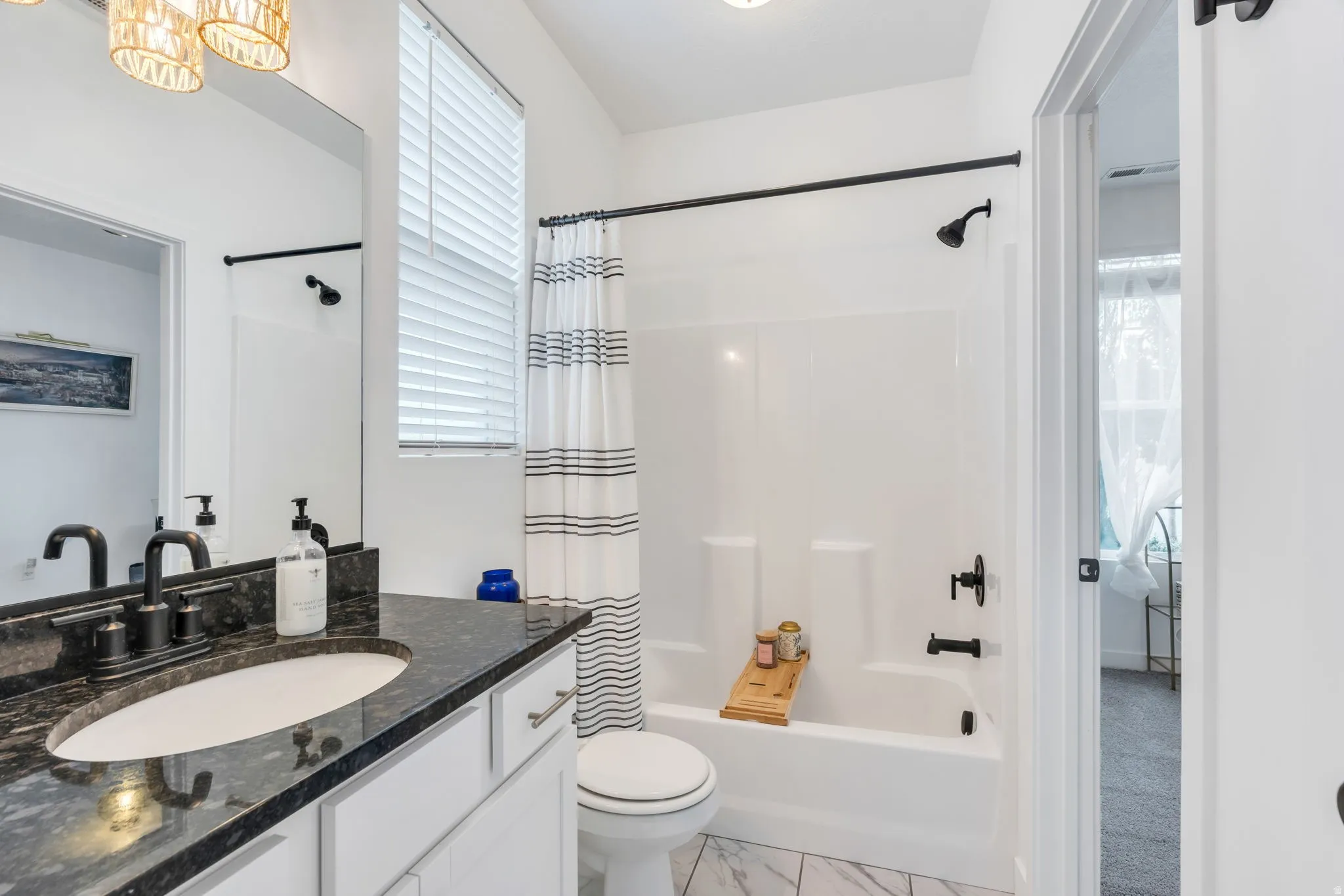 Bathroom featuring a dark stone-finish vanity with an undermount sink, matte black fixtures, a built-in tub with shower, and white tile flooring