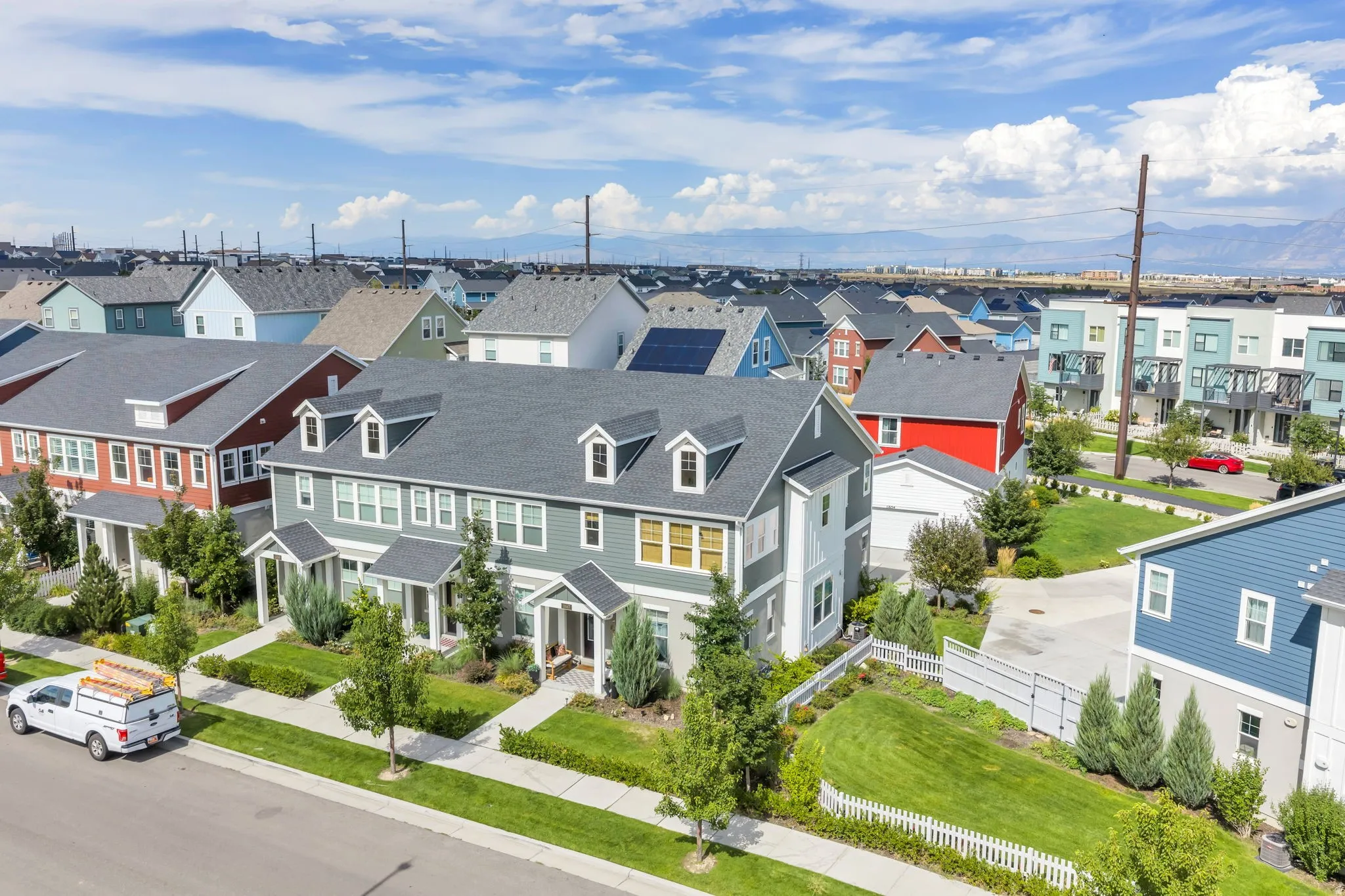 Townhome exterior featuring dormer windows, covered entryways, a manicured lawn, and paved walkways
