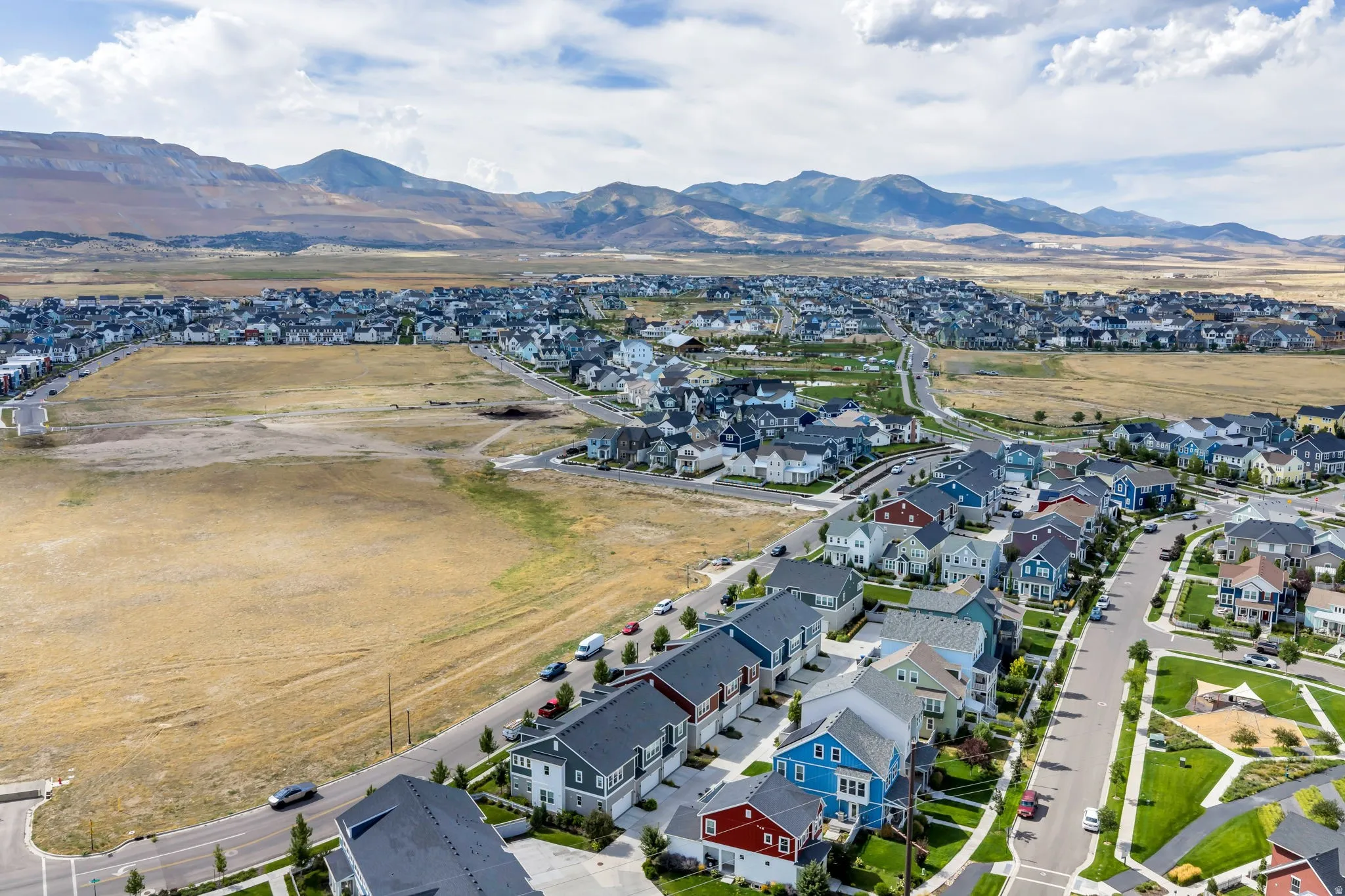 Residential community with varied architectural styles, paved streets, and green spaces, set against a mountainous backdrop