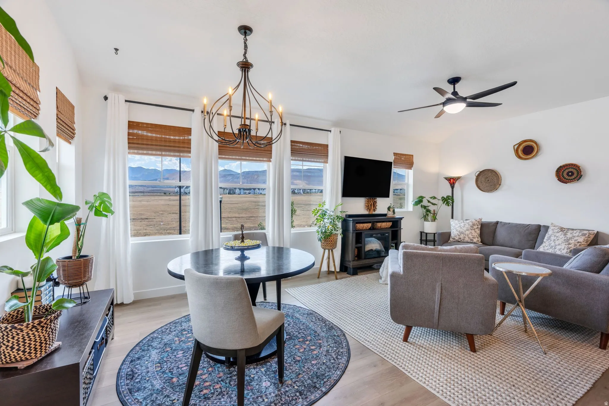 Open-concept living area with wood-finish flooring, a contemporary chandelier, multiple large windows, a built-in electric fireplace, and a ceiling fan