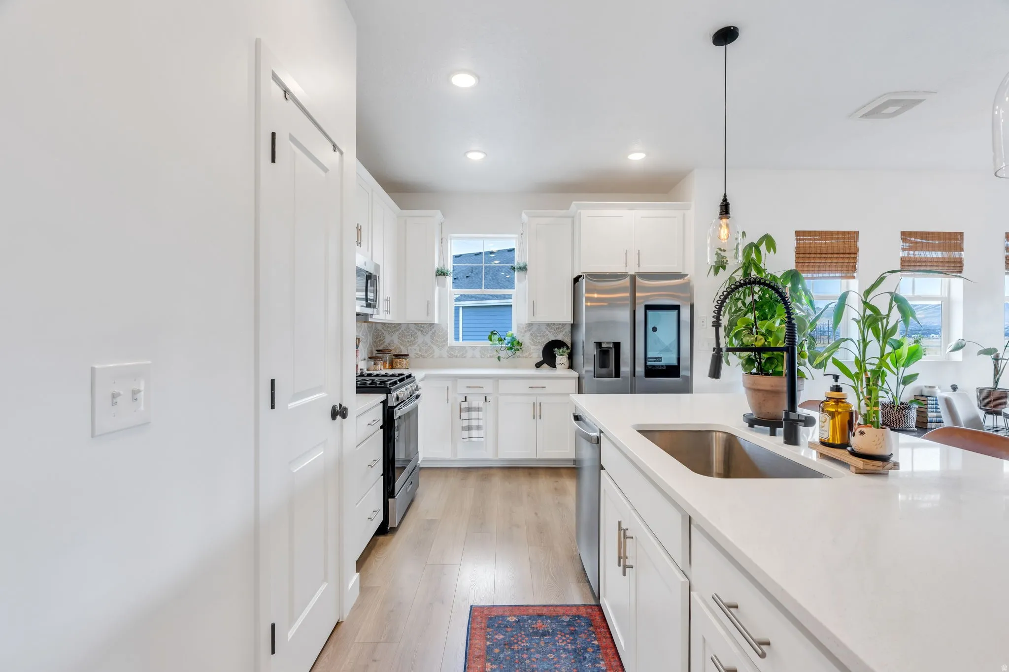 White cabinetry, stainless steel appliances, light wood-finish flooring, white countertops, and a stainless steel sink with a matte black faucet