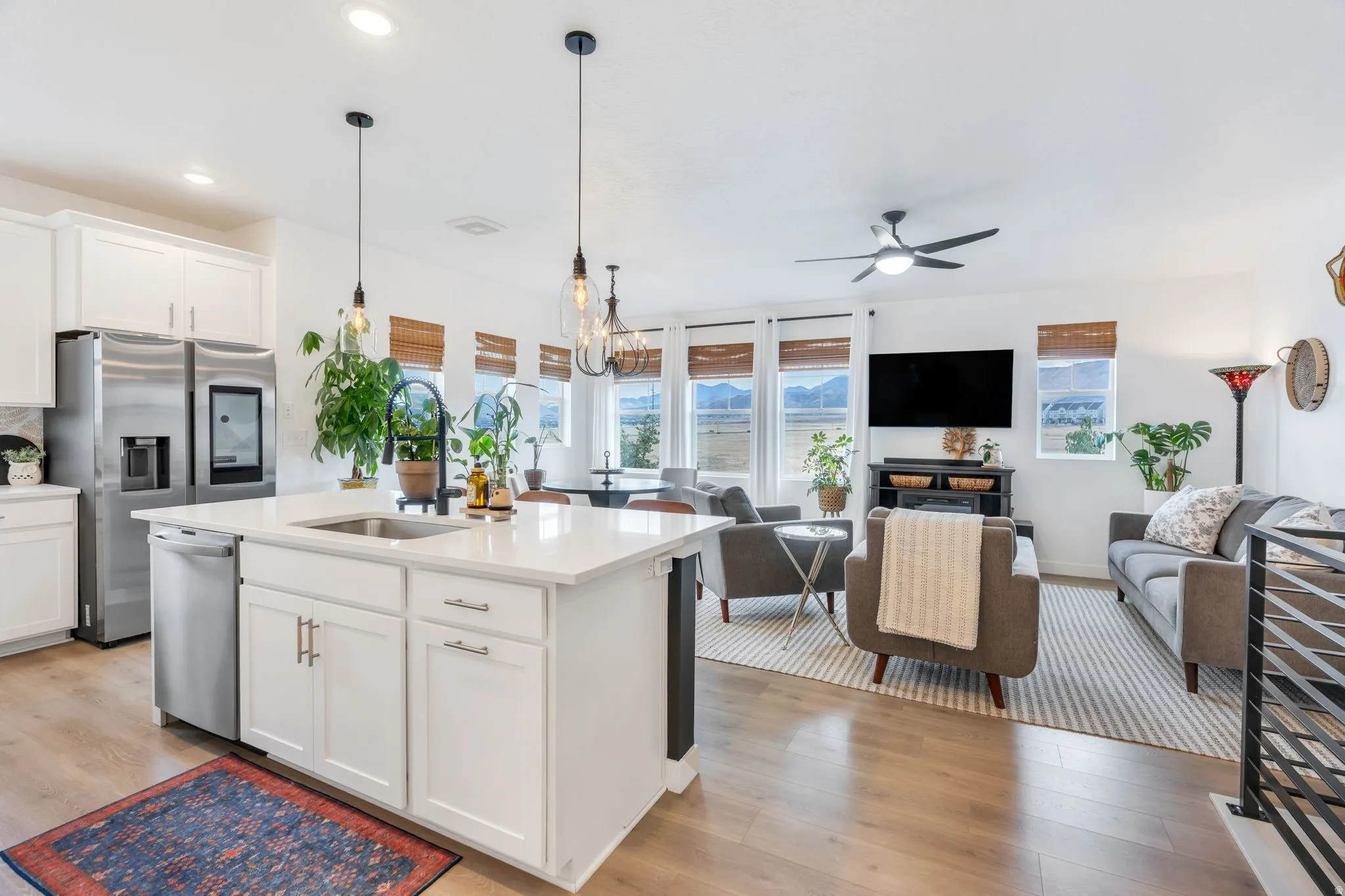 Open-concept living area with wood-finish flooring, white cabinetry, stainless steel appliances, and a kitchen island with sink