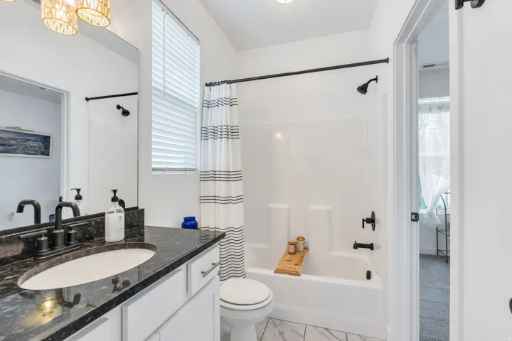Bathroom featuring a dark stone-finish vanity with an undermount sink, matte black fixtures, a built-in tub with shower, and white tile flooring