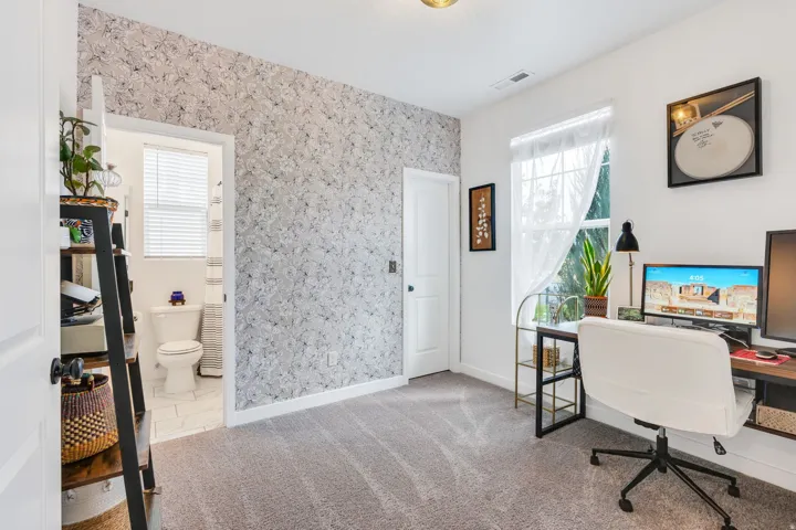 Carpeted room with a wallpaper accent wall, white painted walls, and a window with natural light