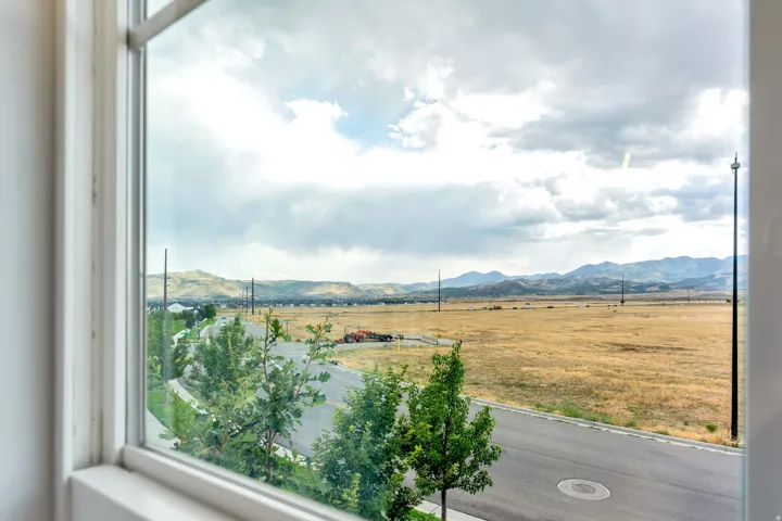 Window with white frame, showcasing a distant mountain range and a large open field