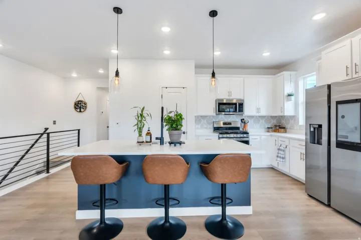 Kitchen featuring a spacious island with a white countertop, white cabinetry with stainless steel appliances, a decorative tile backsplash, wood-finish flooring, and pendant lighting