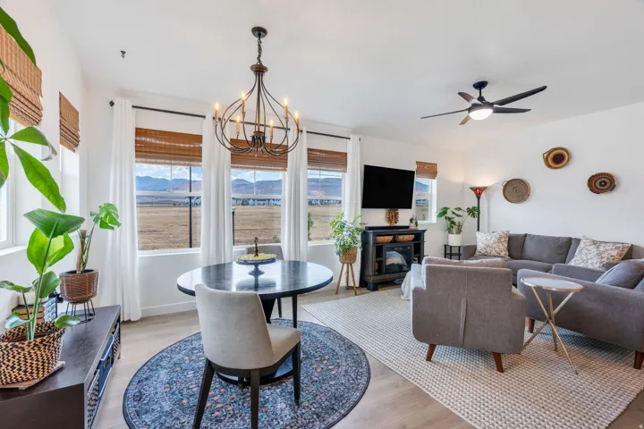 Open-concept living area with wood-finish flooring, a contemporary chandelier, multiple large windows, a built-in electric fireplace, and a ceiling fan
