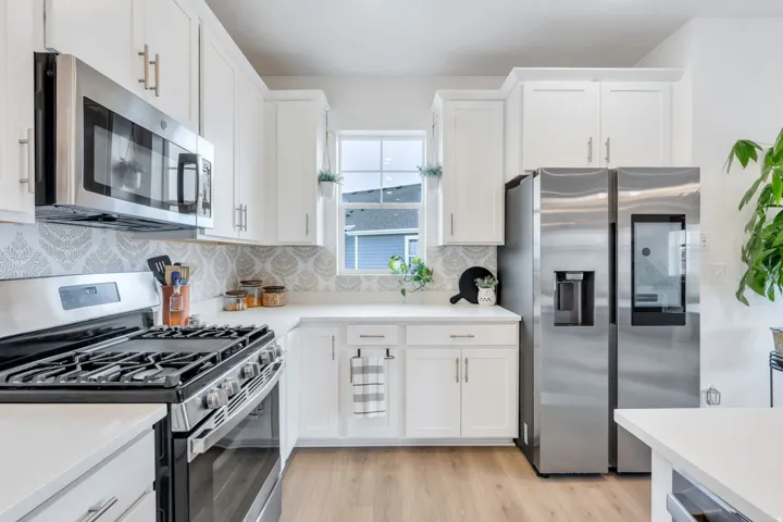 White shaker-style cabinetry, stainless steel appliances, patterned tile backsplash, light wood-finish flooring, and white countertops