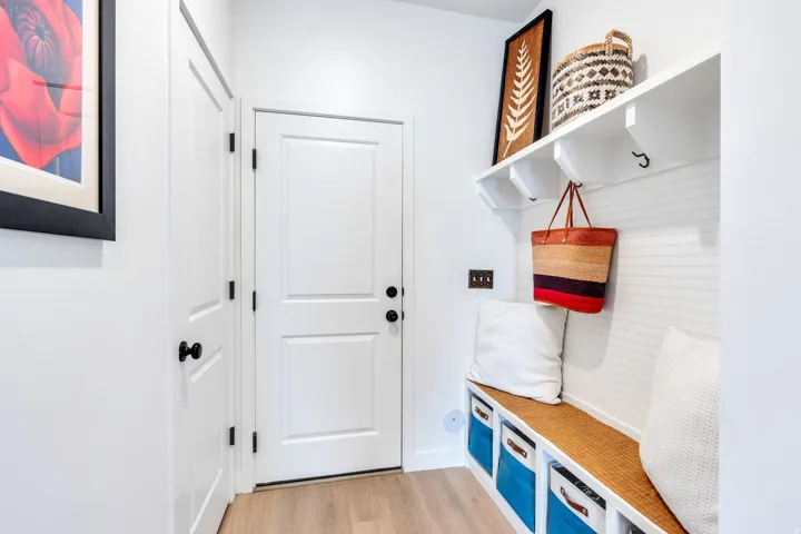 Built-in mudroom bench with storage, white paneled walls, light wood-finish flooring, and white trim