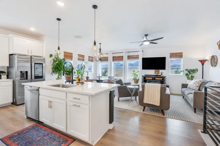 Open-concept living area with wood-finish flooring, white cabinetry, stainless steel appliances, and a kitchen island with sink