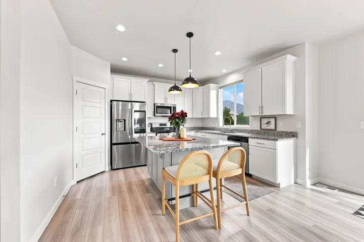 Kitchen featuring a central island with a granite countertop, white cabinetry, stainless steel appliances, and wood-finish flooring