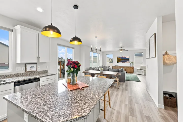 Kitchen with granite countertops, stainless steel dishwasher, white cabinetry, and pendant lighting