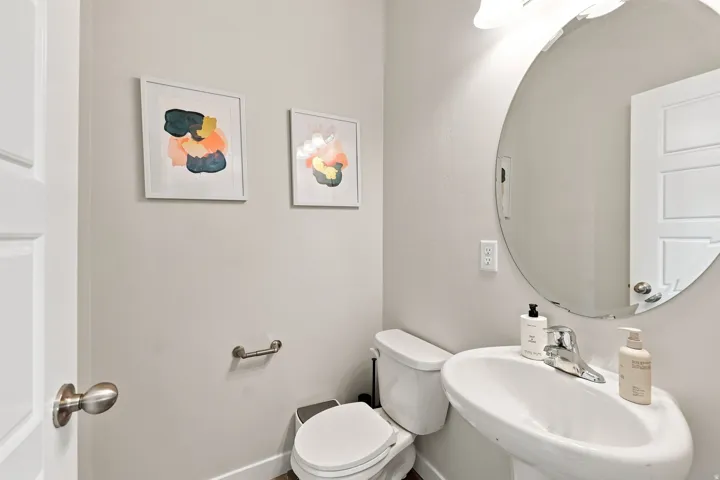 Pedestal sink with chrome faucet, circular mirror, and wall-mounted lighting fixture
