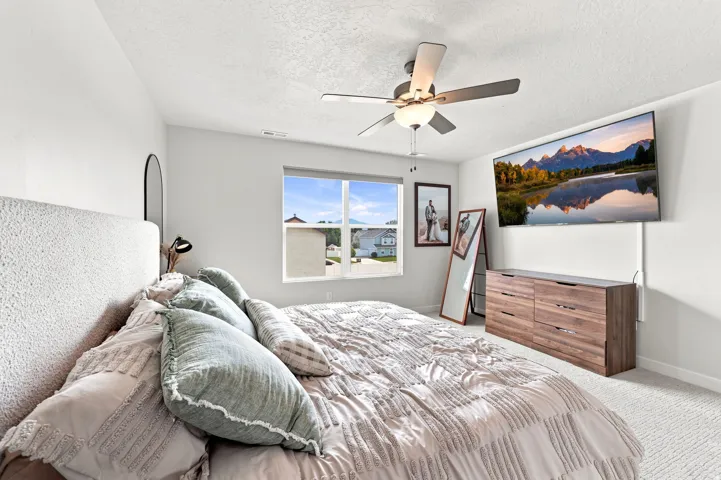 Wall-mounted television with visible cabling, wood-finish dresser, window, and a ceiling fan