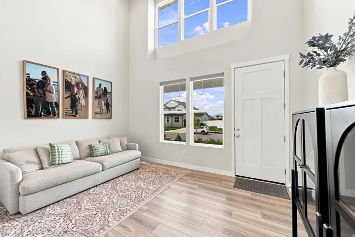 Vaulted ceiling with high windows, light wood-finish flooring, white walls, and a white entry door with frosted glass panels