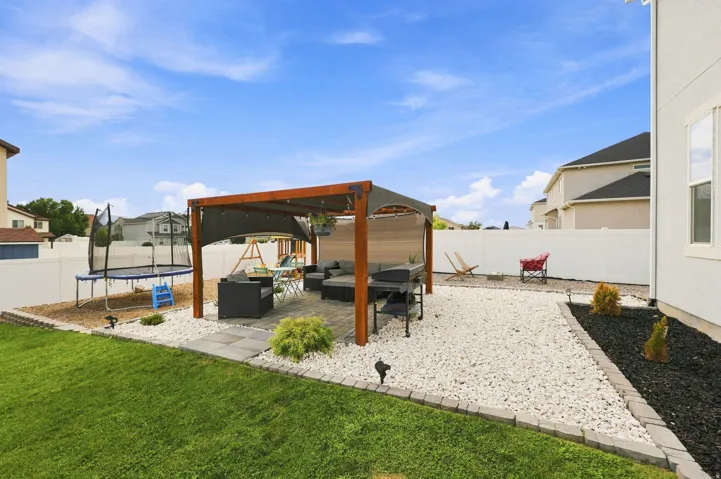 Expansive backyard featuring a covered patio, paved square patio, white privacy fencing, and a manicured lawn