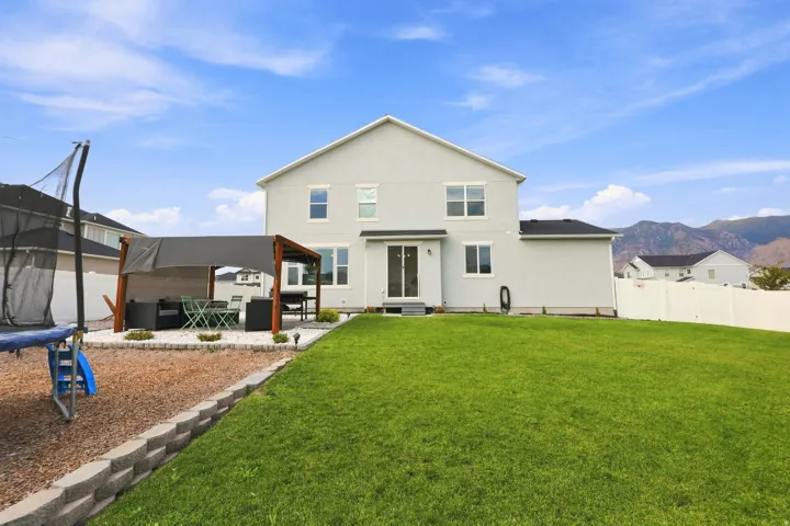 Expansive backyard featuring a manicured lawn, a retaining wall, a wood pergola, and a white vinyl fence