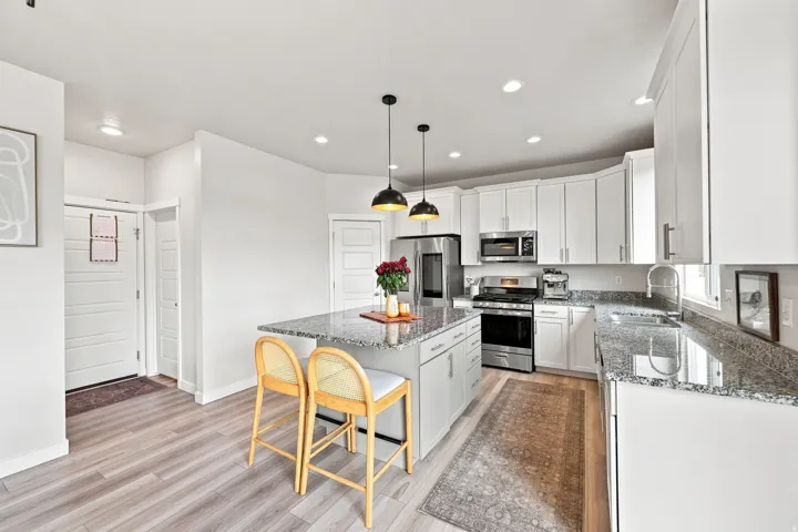 Kitchen featuring a gray island with granite countertop, stainless steel appliances, white cabinetry, wood-finish flooring, and recessed lighting