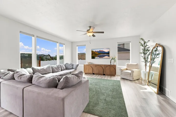Spacious interior with expansive windows, light wood-finish flooring, a ceiling fan, and a built-in wood-tone media console