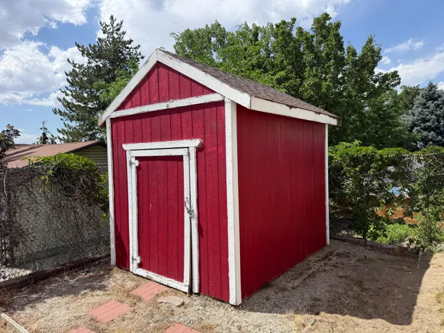 Charming red garden shed featuring white trim accents, peaked roof design, and single entry door