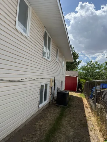 Siding exterior with multiple windows, featuring an air conditioning unit and a detached red shed