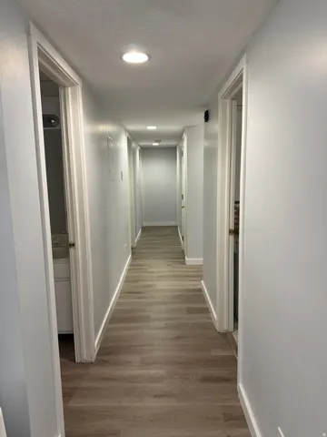 Recessed lighting illuminates the hallway, featuring wood-finish flooring and light-toned walls
