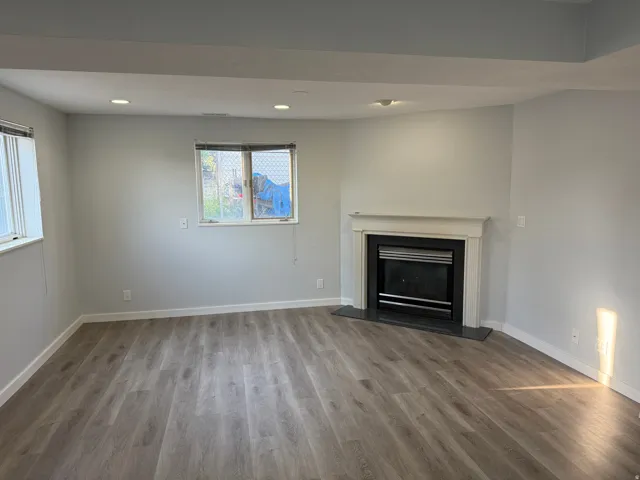 Recessed lighting, wood-finish flooring, and a fireplace with a white mantel and dark hearth