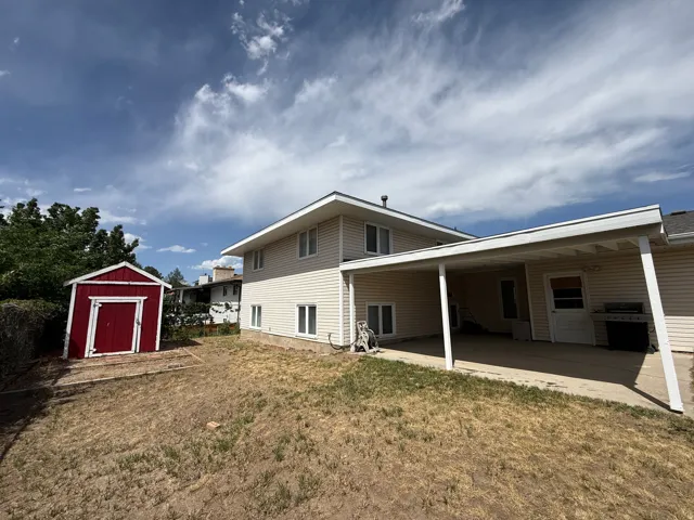 Rear exterior featuring a covered patio, neutral-toned siding, multiple windows, and a red shed