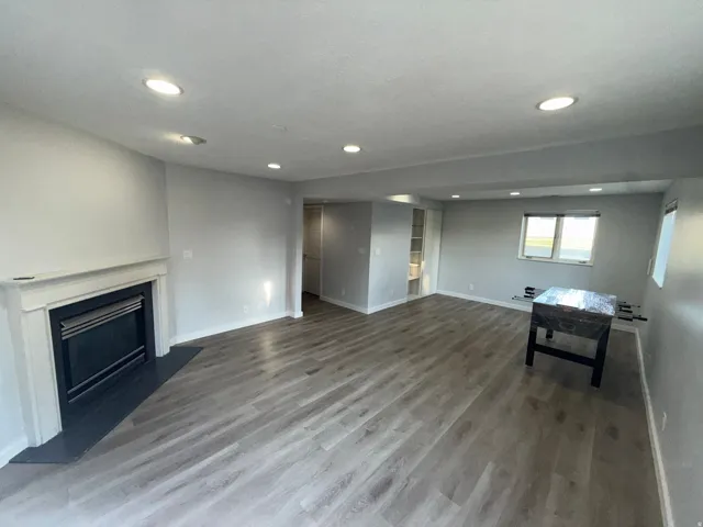 Recessed lighting throughout, wood-finish flooring, fireplace with a white mantel and dark hearth, built-in shelving, and multiple windows