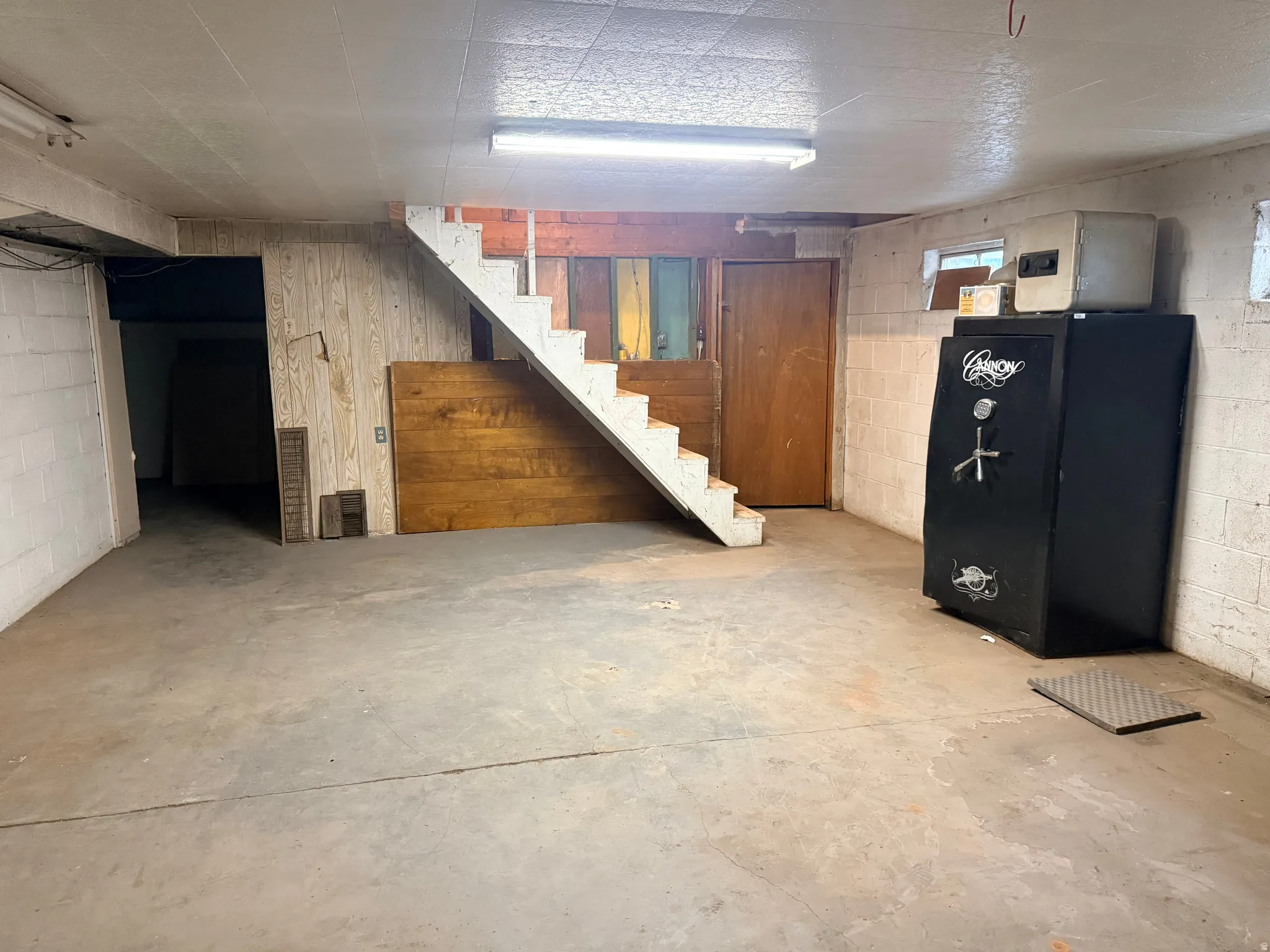 Concrete flooring, painted cinder block walls, wood-finish paneling, exposed staircase, and fluorescent lighting